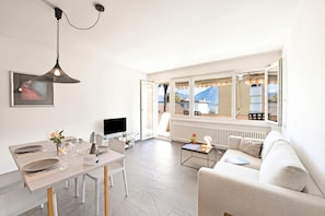 Ein modernes Wohnzimmer mit Essbereich, einer Couch, einem Fernseher und einem Fenster mit Bergblick.