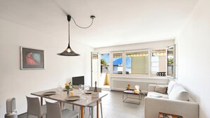 A modern living room with a dining area, a sofa, a coffee table, and a radiator. - Malibu46 - Minusio Apt With Shared Pool & Balcony (Minusio)