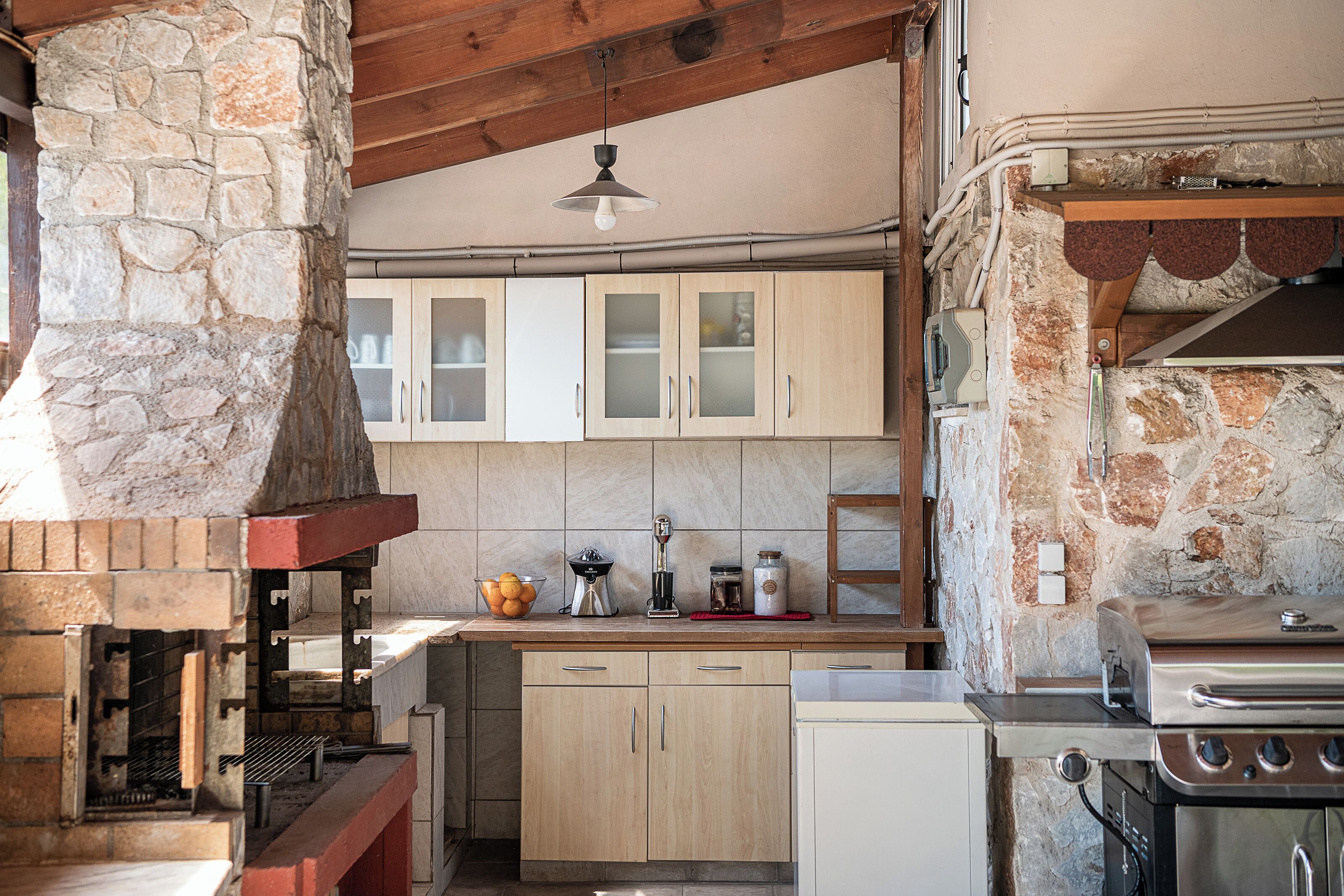 Una cocina con paredes de piedra, armarios de madera, una parrilla empotrada y una chimenea de piedra.