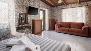 A room with a stone wall, a wooden ceiling, a television, a sofa, a chair, a bed with towels, and a dresser.