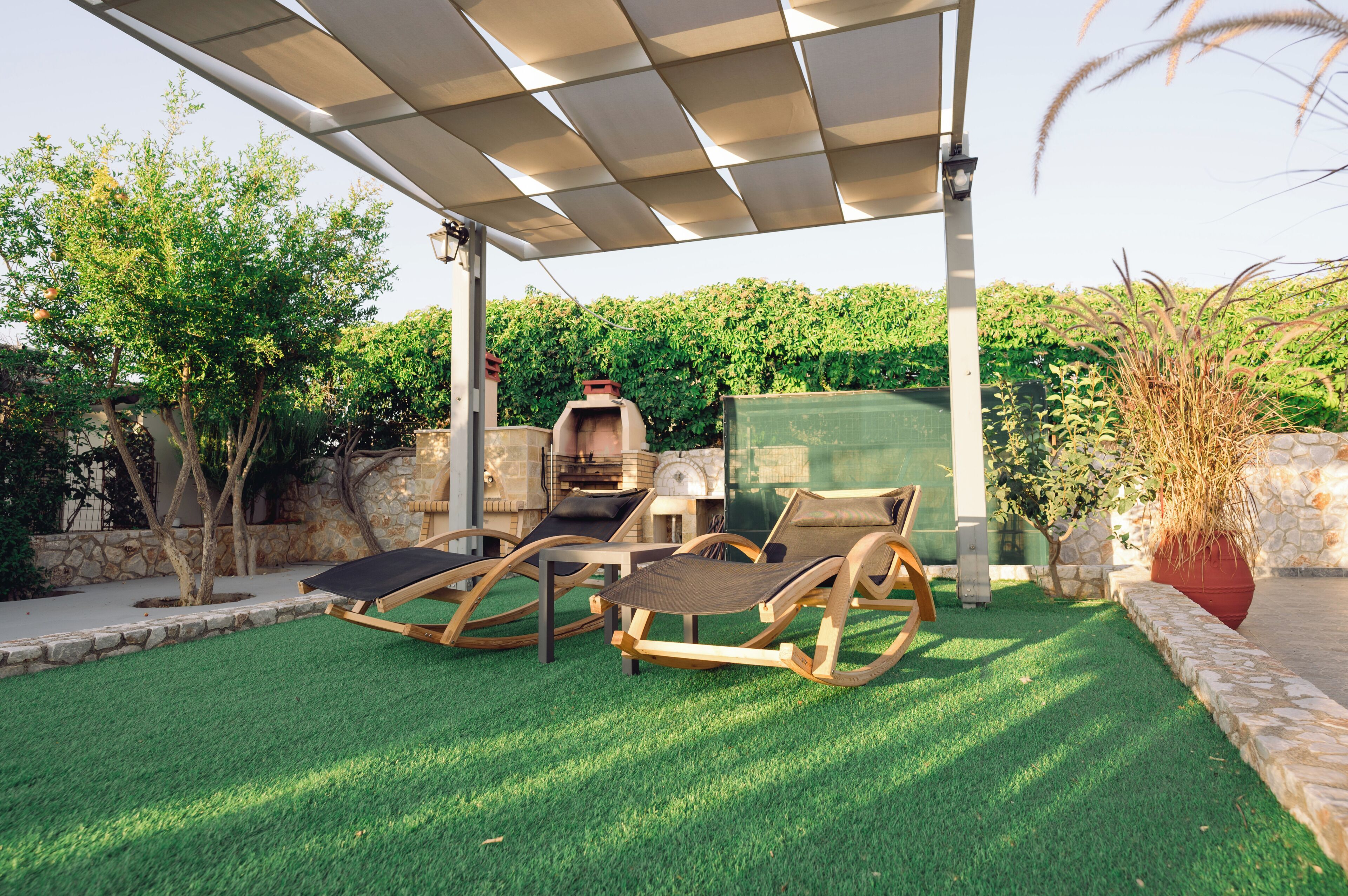 A patio with two rocking chairs, a barbecue grill, and a pergola.