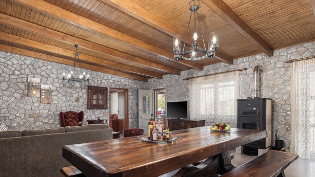 A spacious living area with a large wooden table, stone walls, and a stone fireplace.