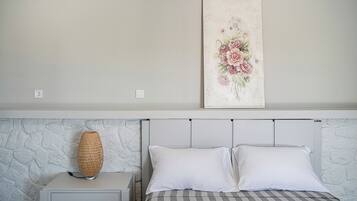 Un dormitorio con una cama, dos almohadas, una mesita de noche, una lámpara y una obra de arte floral en la pared.