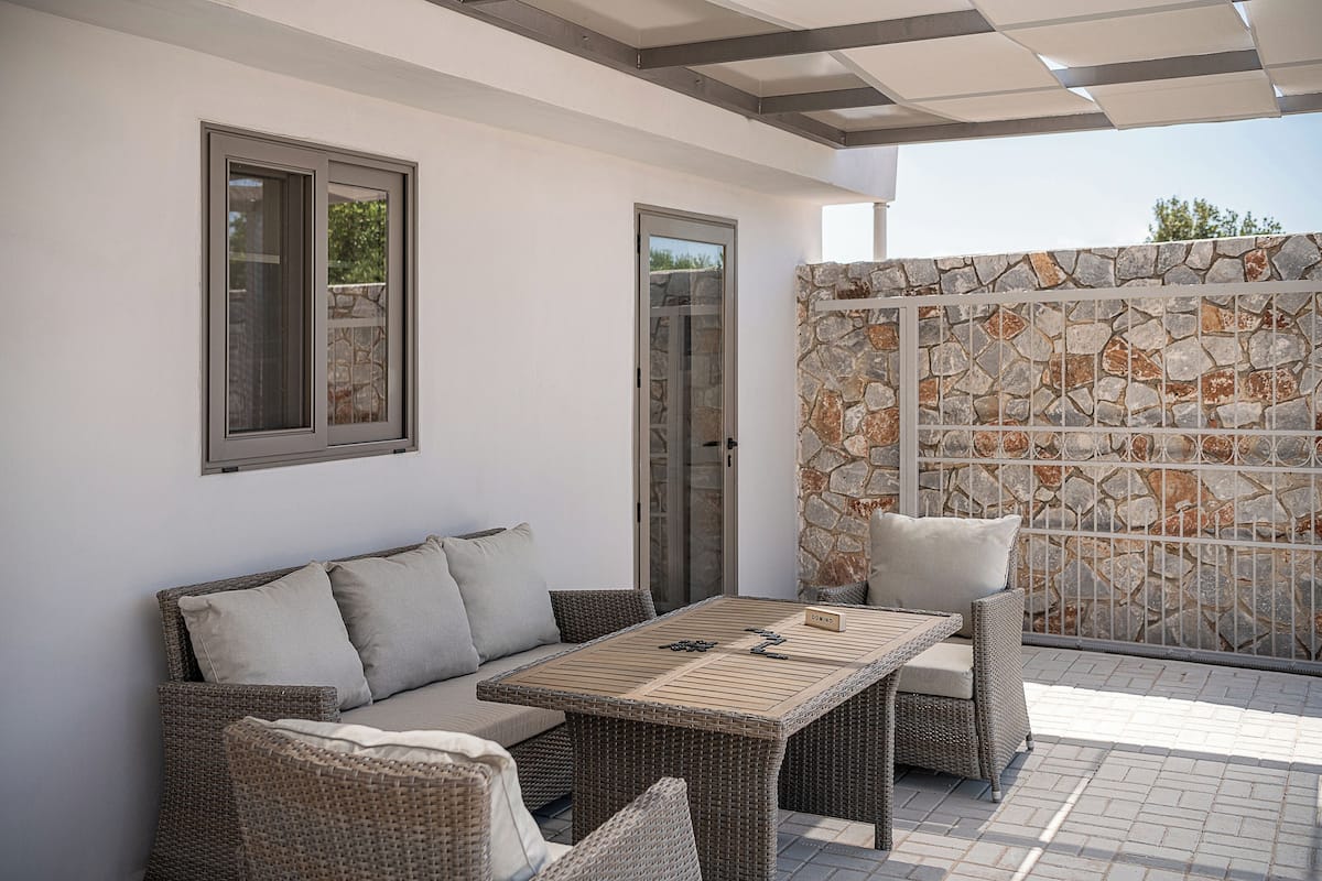 A patio area with a wicker sofa, a table, and a stone wall.