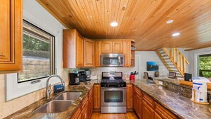 A kitchen with wooden cabinets, stainless steel appliances, a granite countertop, and a window overlooking a stone wall. - On the Rocks: Riverside Relaxation Awaits (Sevierville)