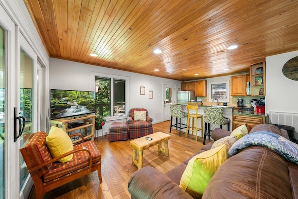 A cozy living room with a wooden ceiling, a television, and a sofa with cushions. - On the Rocks: Riverside Relaxation Awaits (Sevierville)