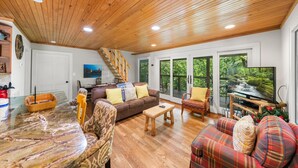 A spacious living room with a wooden ceiling, a large TV, and a cozy seating area with a couch and chairs. - On the Rocks: Riverside Relaxation Awaits (Sevierville)
