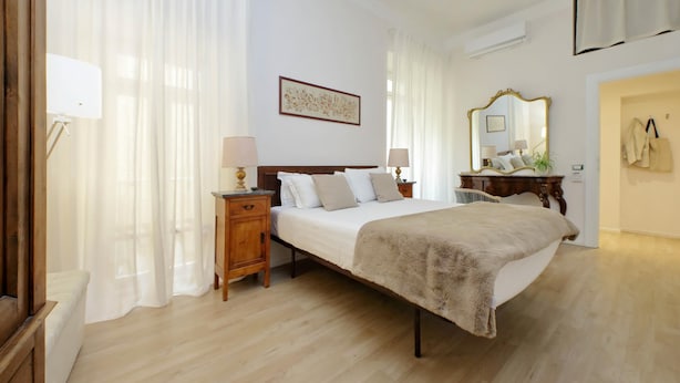 A bedroom with a wooden bed, bedside tables with lamps, a mirror, and a painting on the wall. - Treasurerome Opera Trevi Green Suite 2BR (Rome)