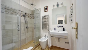 A modern bathroom with a glass-enclosed shower, a bidet, a sink, and a mirror. - Treasurerome Opera Trevi Green Suite 2BR (Rome)
