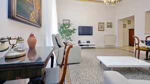 A living room with a sofa, a television, a chandelier, and a painting on the wall. - Treasurerome Opera Trevi Green Suite 2BR (Rome)