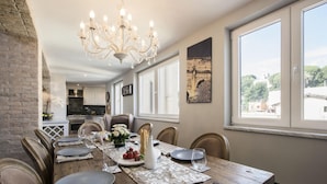 Un coin repas avec une table en bois dressée pour six personnes, entourée de chaises, d’un lustre et offrant une vue sur la ville grâce à de grandes fenêtres.