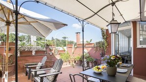 Une terrasse avec des sièges d’extérieur, une table avec des aliments pour le petit-déjeuner et des plantes en pot.