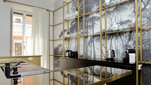A modern kitchen with a black countertop, stainless steel appliances, and a glass shelf unit with kitchenware. - Treasurerome Quattro Fontane Luxury (Rome)