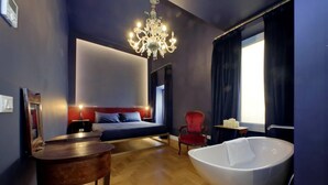 A modern bedroom with a large bed, a red chair, a wooden table, and a freestanding bathtub. - Treasurerome Quattro Fontane Luxury (Rome)