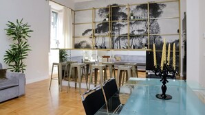 A modern living room with a glass dining table, a grey sofa, and a large abstract painting on the wall. - Treasurerome Quattro Fontane Luxury (Rome)