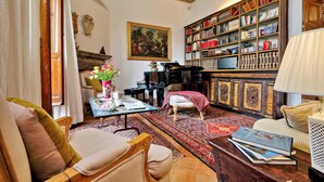 A cozy living room with a piano, a large bookshelf, and a comfortable seating area. - Treasurerome Colosseum Terrace 2BR (Rome)
