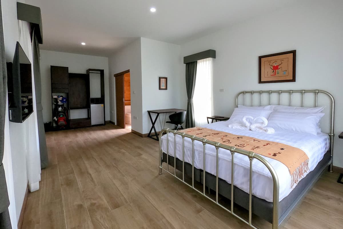 A hotel room with a metal-framed bed, a desk, a chair, a small table, and a television mounted on the wall.