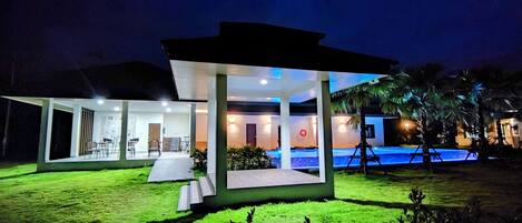 Una casa moderna con un porche cubierto, piscina y césped cuidado.