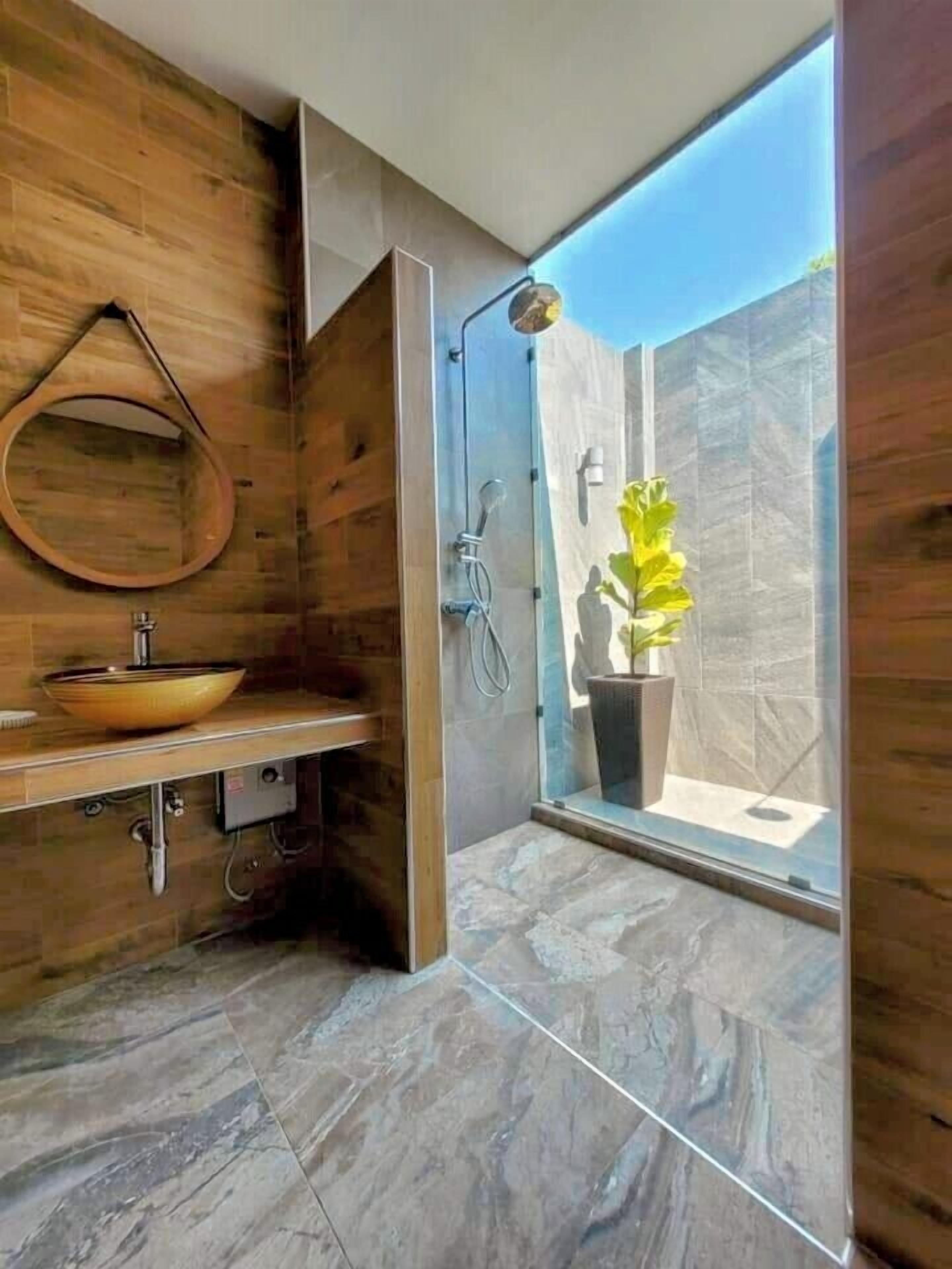 Un baño moderno con tocador de madera, un lavamanos redondo y una ducha con puerta de cristal.