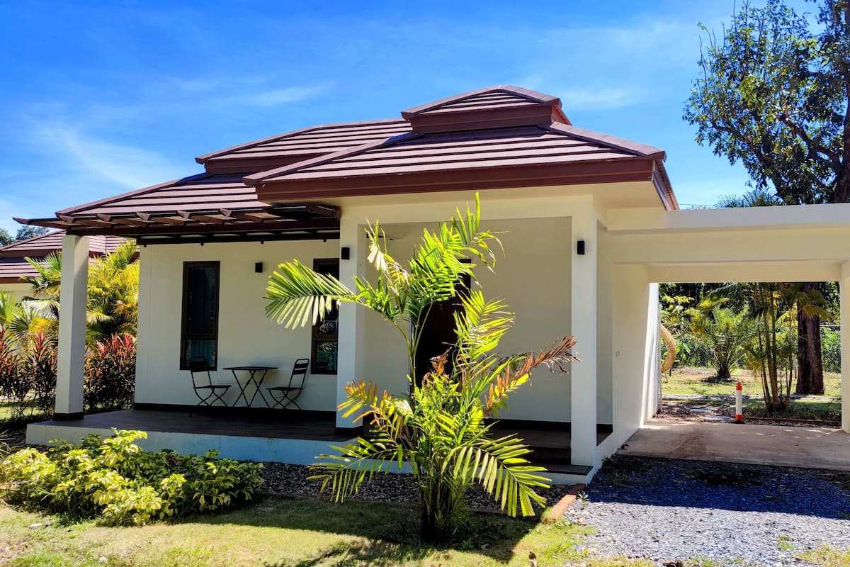 A two-story house with a covered patio, a small garden, and a view of the surrounding greenery.