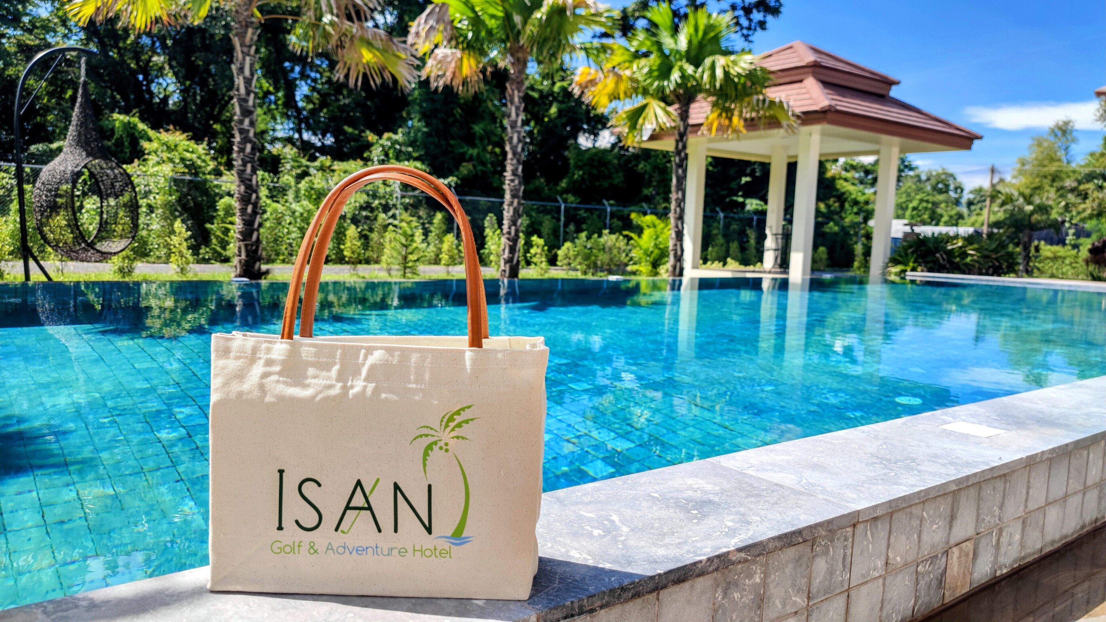 Blick über den Pool mit einer Tasche mit dem Aufdruck "ISAN Golf & Adventure Hotel" und einer Laube im Hintergrund.
