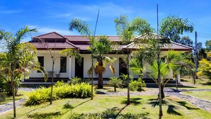 A two-story house with a red roof, surrounded by tropical vegetation and a clear blue sky. - Isan Golf & Adventure Hotel (Phen)