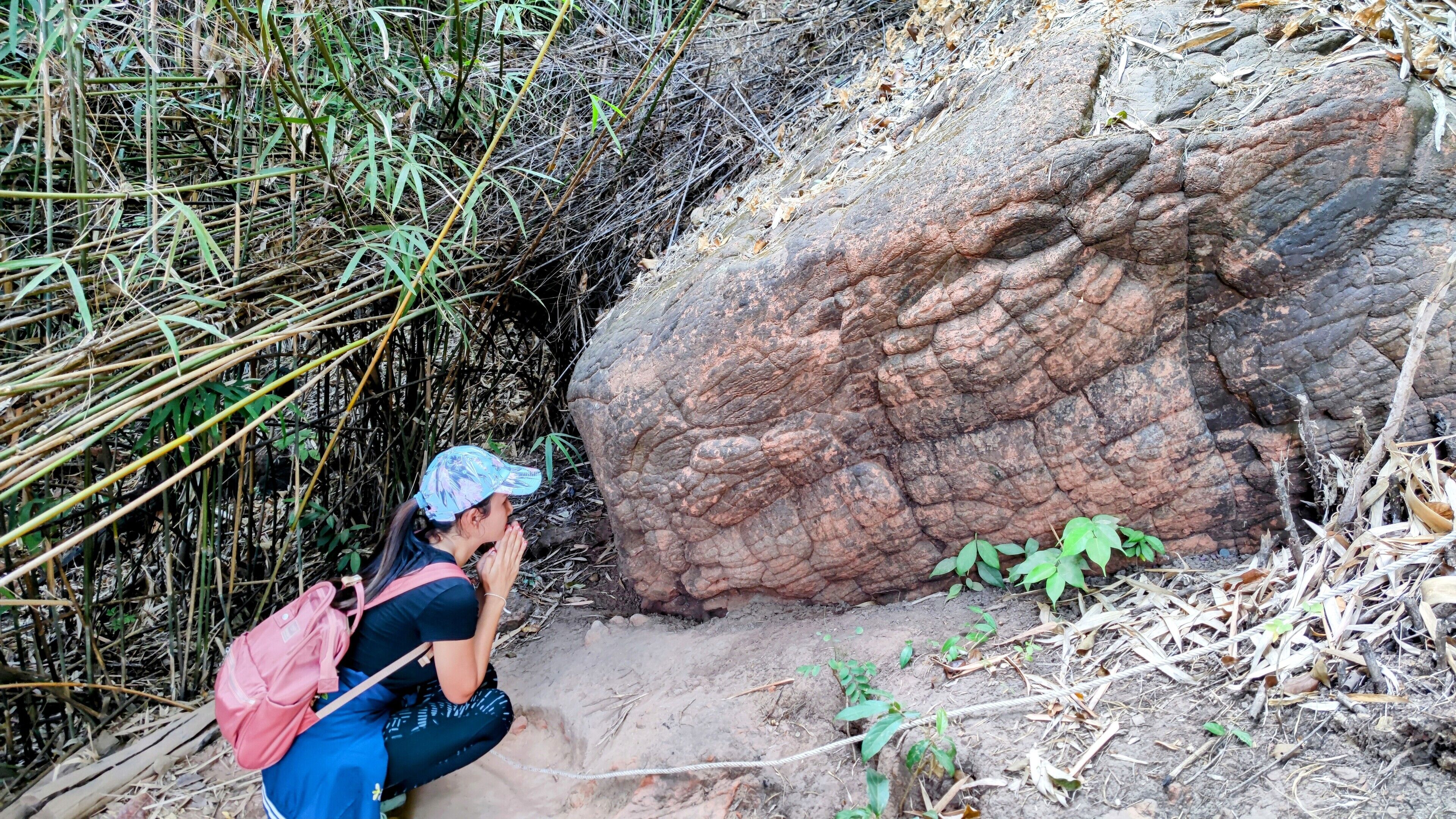 A person crouching next to a large rock formation in a natural setting.