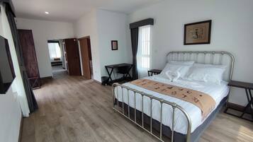 Un dormitorio con estructura de cama metálica, suelo de madera, un escritorio con silla y una ventana con cortinas.