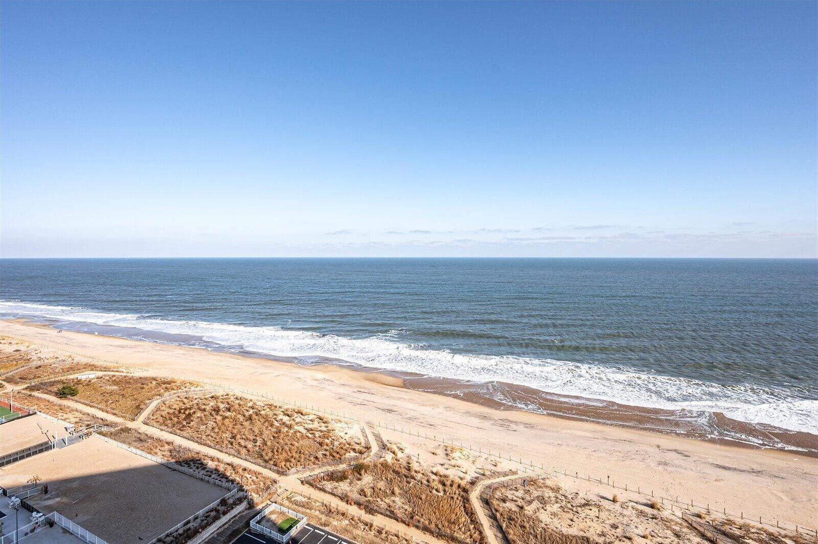 A beach with a sandy path leading to the ocean, a fenced area, and a small green structure.