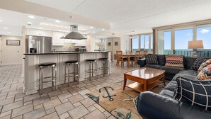 A spacious living area with a kitchen, bar stools, a dining table, and a sofa with patterned cushions.