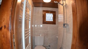 Ein kleines Badezimmer mit Holzpaneelen, einer Toilette, einer Dusche und einem kleinen Fenster.