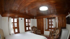 Ein Zimmer mit Holzwänden, einem Bett, zwei Sesseln, einem Kühlschrank und einer Kristallleuchtre.