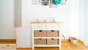 A white cabinet with wicker baskets, a wooden floor, and a white wall with a mirror and three framed pictures.