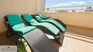 A rooftop terrace with two lounge chairs, a tiled floor, and a view of the city skyline.