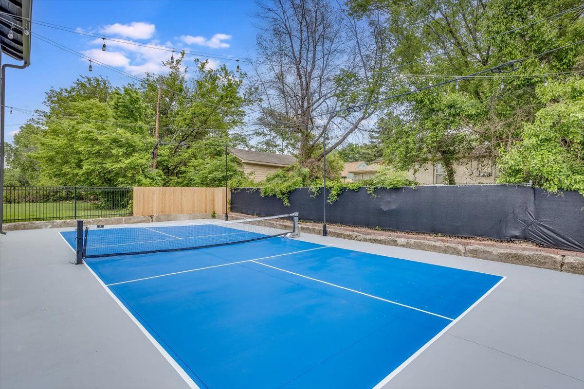 An outdoor tennis court with a blue surface, surrounded by a wooden fence and trees.