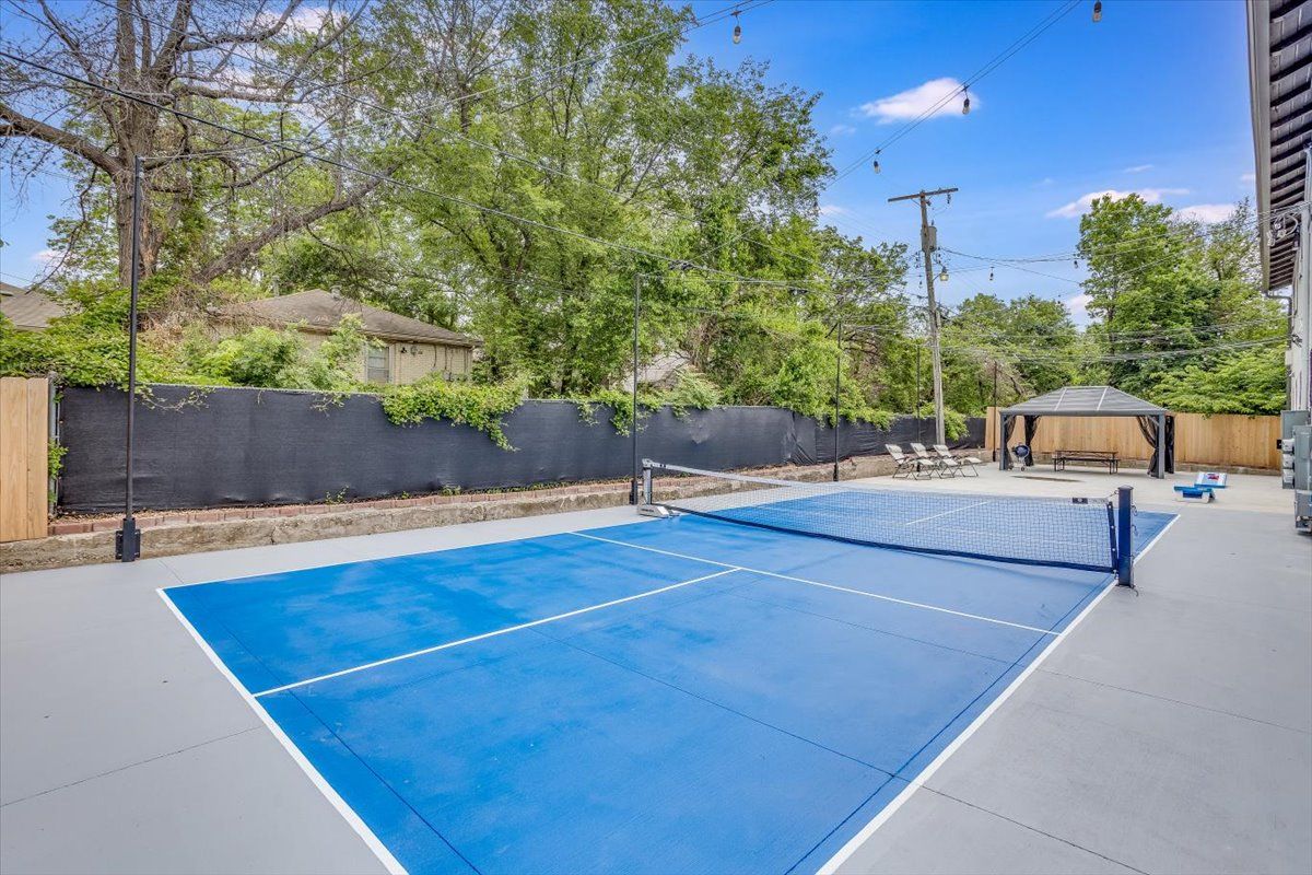 An outdoor tennis court with a net, surrounded by a wooden fence and trees.
