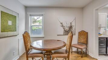 Uma sala de jantar com uma mesa redonda e quatro cadeiras, uma janela com vista e uma pintura de um touro na parede.