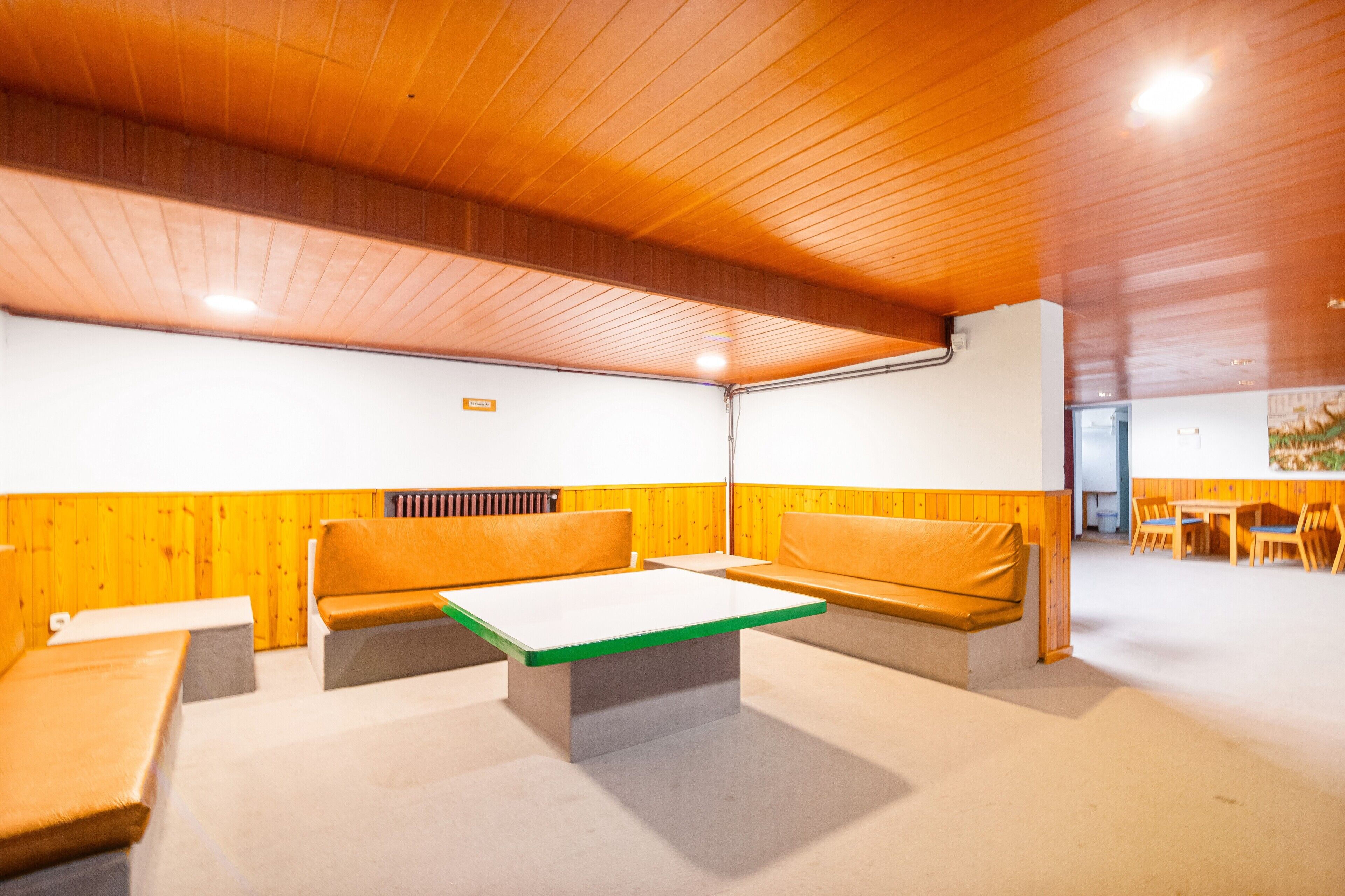 A modern interior with wooden panel walls, a green-topped table, and orange seating.