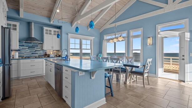 Una cocina amplia con una isla grande, armarios blancos y vista a la playa.