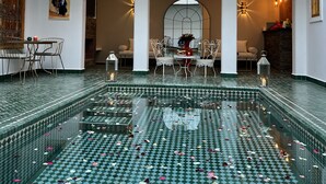 A spacious indoor pool with a green checkered floor, surrounded by white arches and a balcony with a railing. - Riad Darchica (Marrakech)