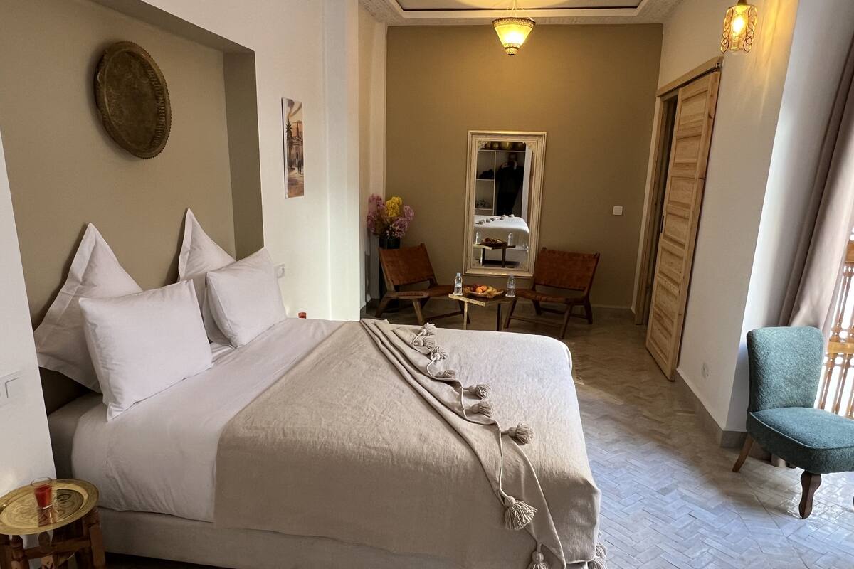 A neatly arranged bedroom with a large bed, a small table with a drink, and a chair.