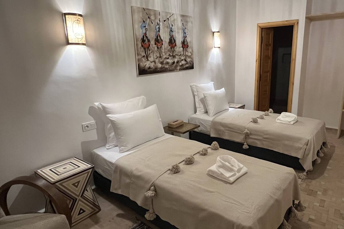 A hotel room with two beds, a painting on the wall, and a wooden wardrobe.