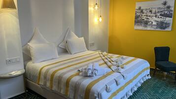 Una habitación de hotel con cama, almohadas, una manta a rayas, una toalla, una silla y un cuadro en la pared.
