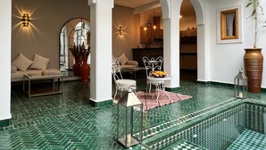 A spacious indoor area with a green tiled floor, white arches, a seating area with cushions, and a dining table with a fruit bowl. - Riad Darchica (Marrakech)