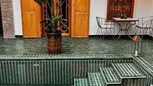 A tiled outdoor area with a wooden door, a potted plant, and a table with chairs. - Riad Darchica (Marrakech)