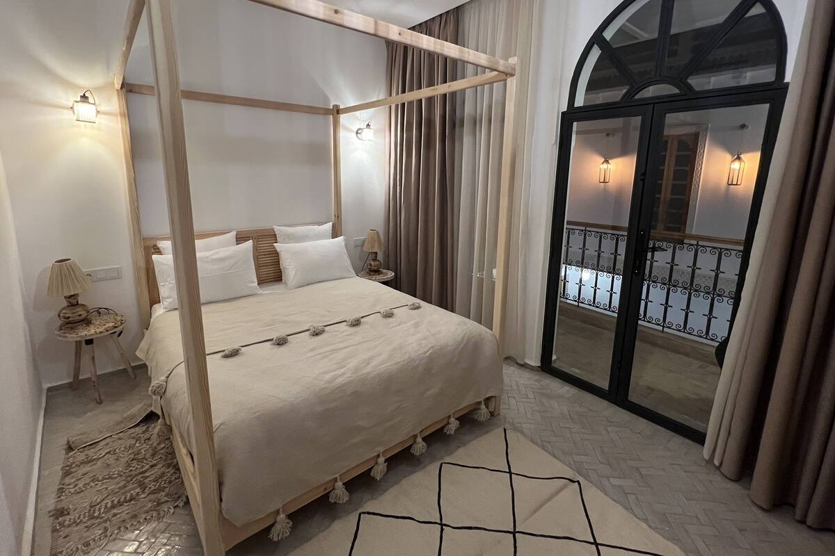 A four-poster bed with a wooden frame, a herringbone-patterned floor, and a view of a balcony with a wrought iron railing.