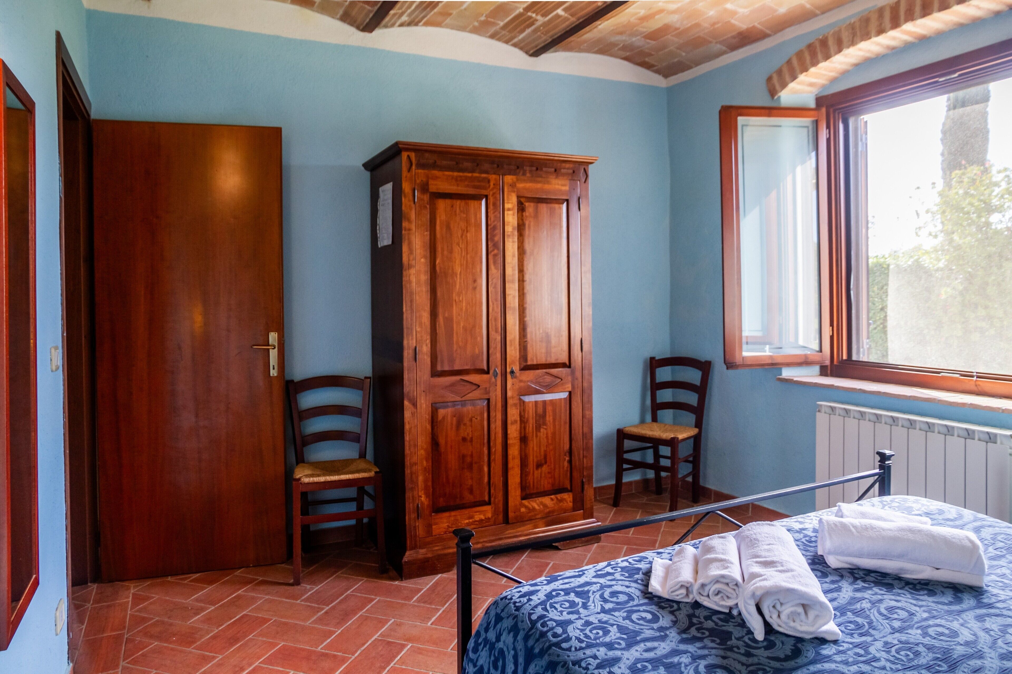 Ein Schlafzimmer mit einem Bett, zwei Stühlen, einem Kleiderschrank und einem Fenster.