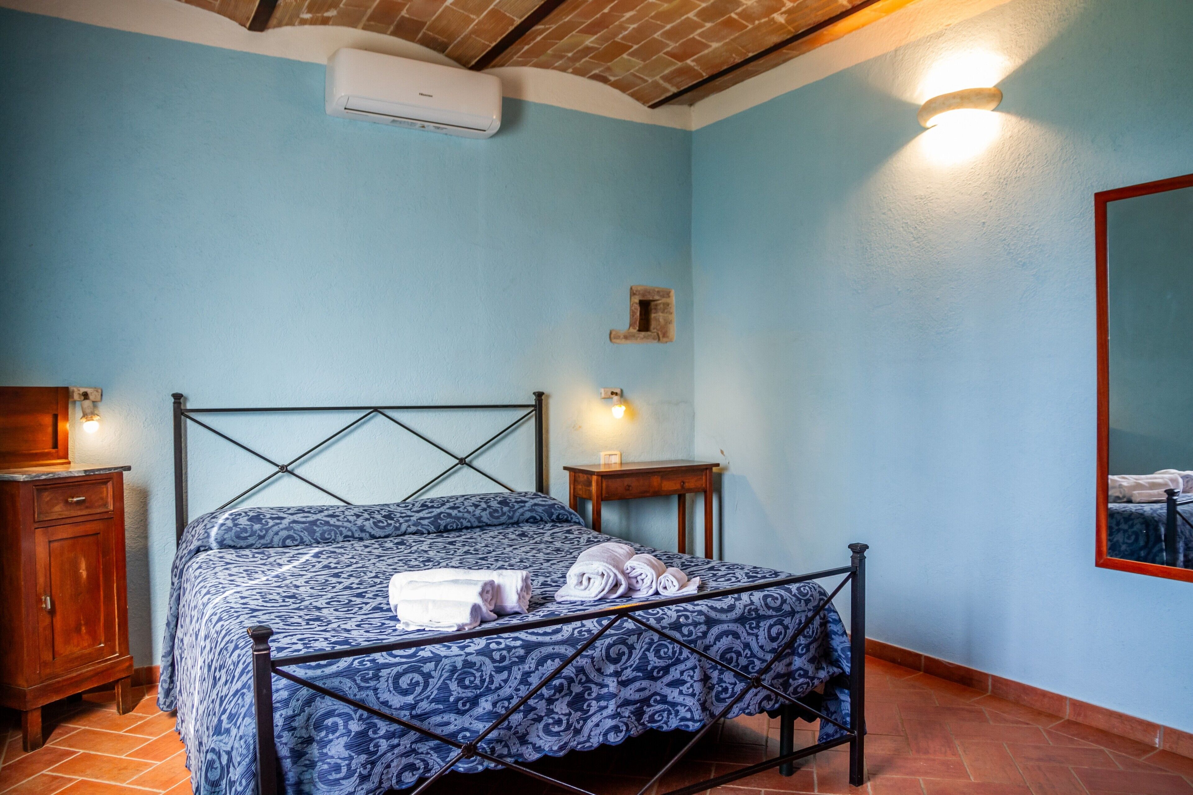 Une chambre à coucher comprenant un lit, une table de chevet en bois, un climatiseur fixé au mur et une petite table avec une lampe.