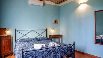 Une chambre à coucher comprenant un lit, une table de chevet en bois, un climatiseur fixé au mur et une petite table avec une lampe.