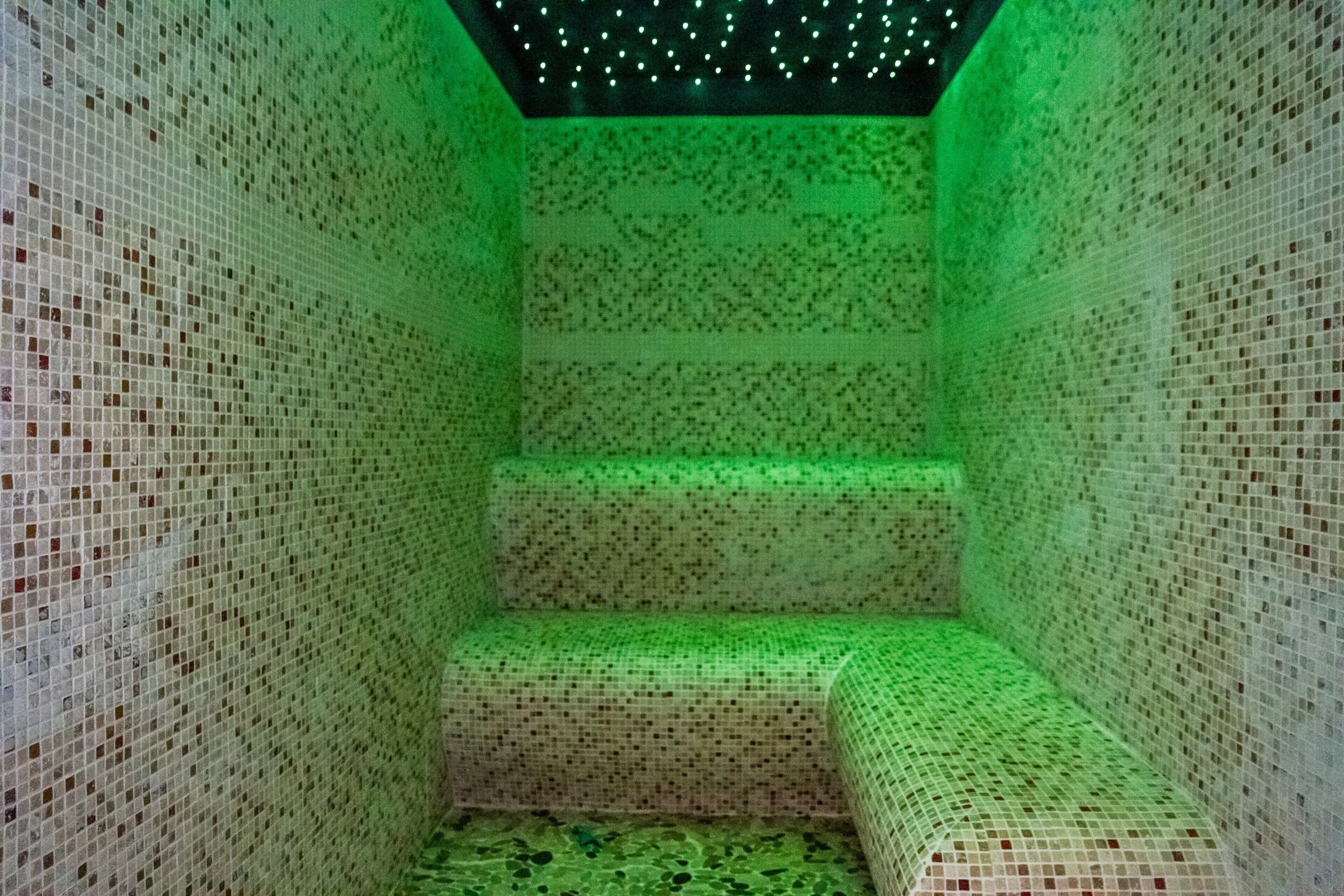 A tiled room with a green-lit ceiling and walls, a bench, and a small step.